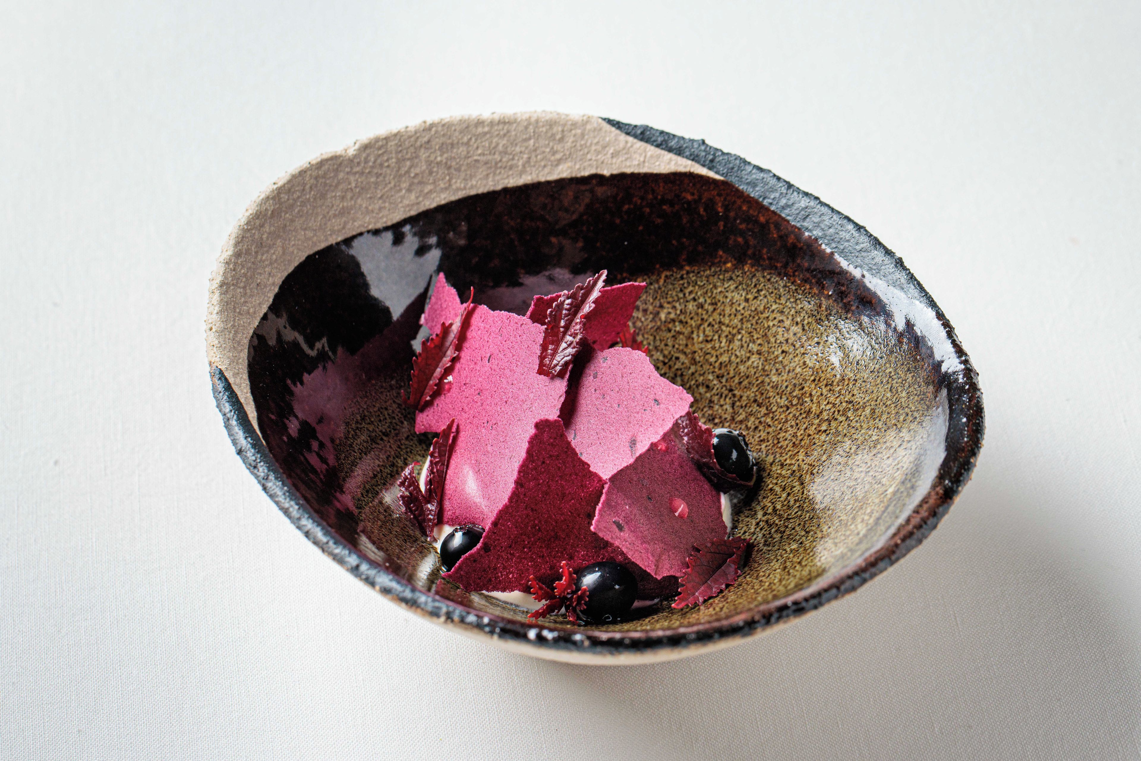 A ceramic bowl with a textured exterior and a dark interior, containing a few red pieces and a black spherical object.
