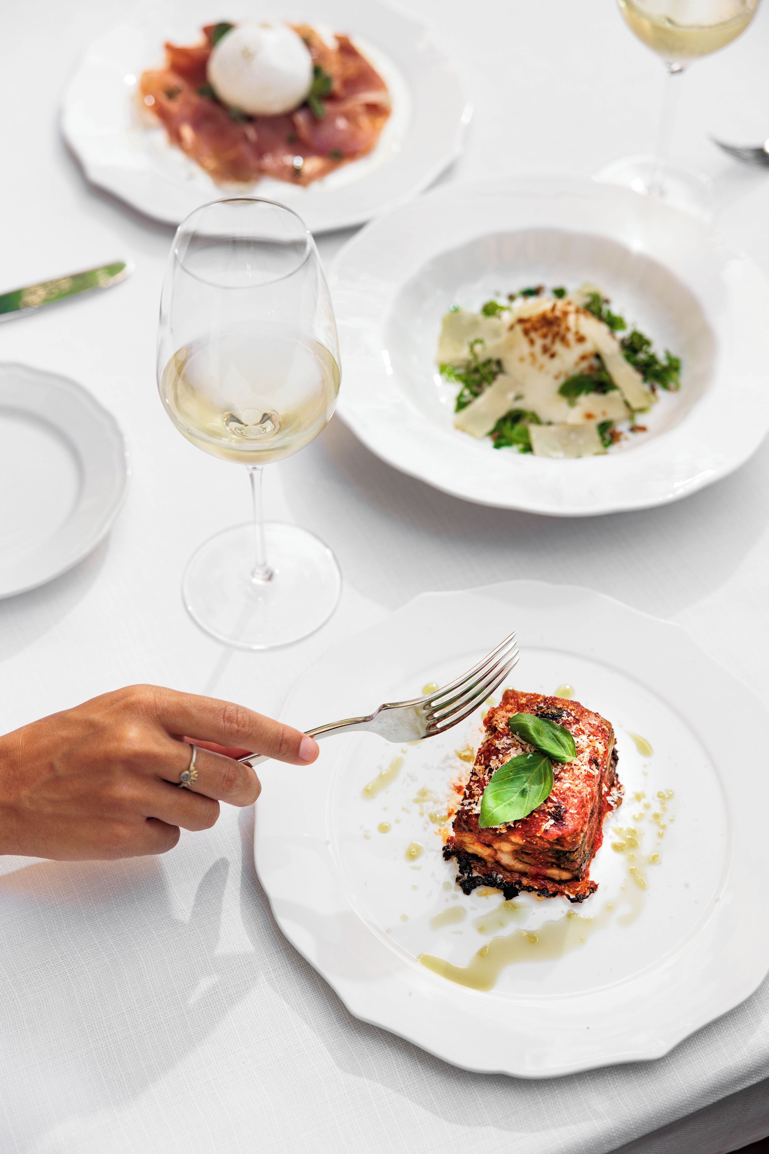 A dining table with plates of food and a wine glass.