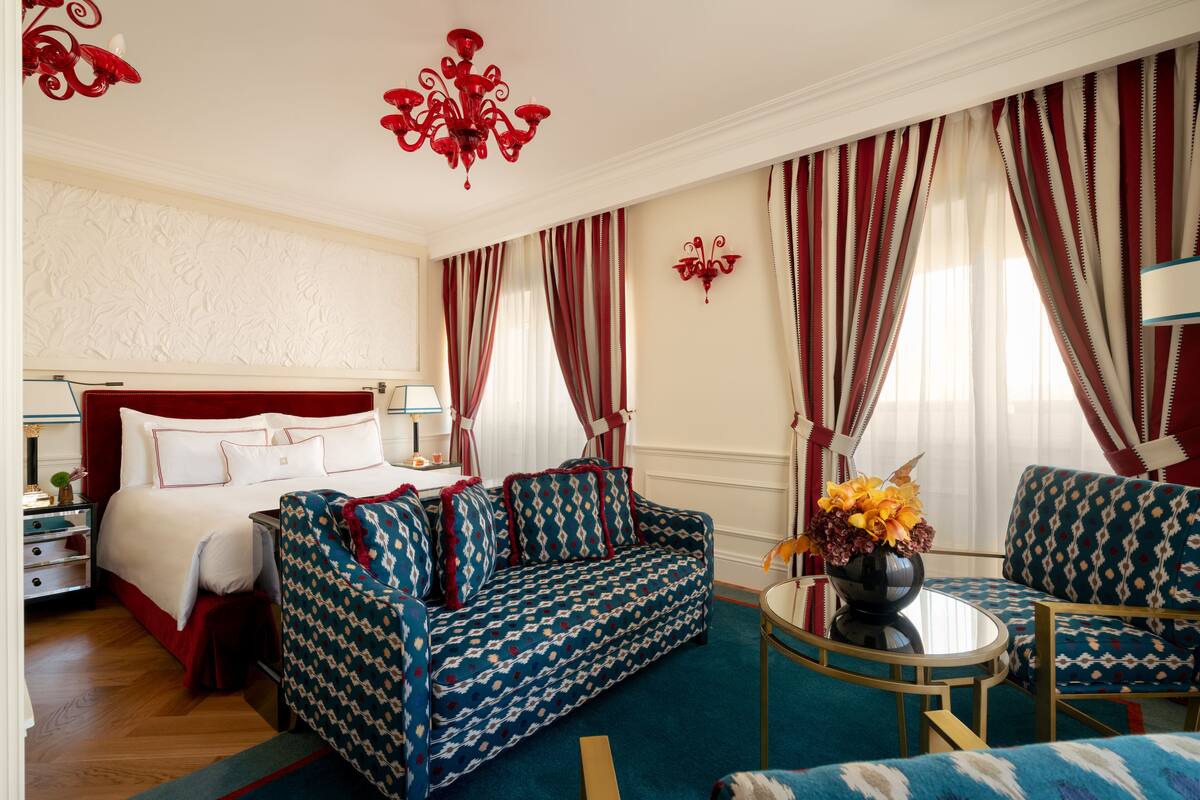A hotel room with a bed, a sofa, a chair, a small table, and a decorative vase.