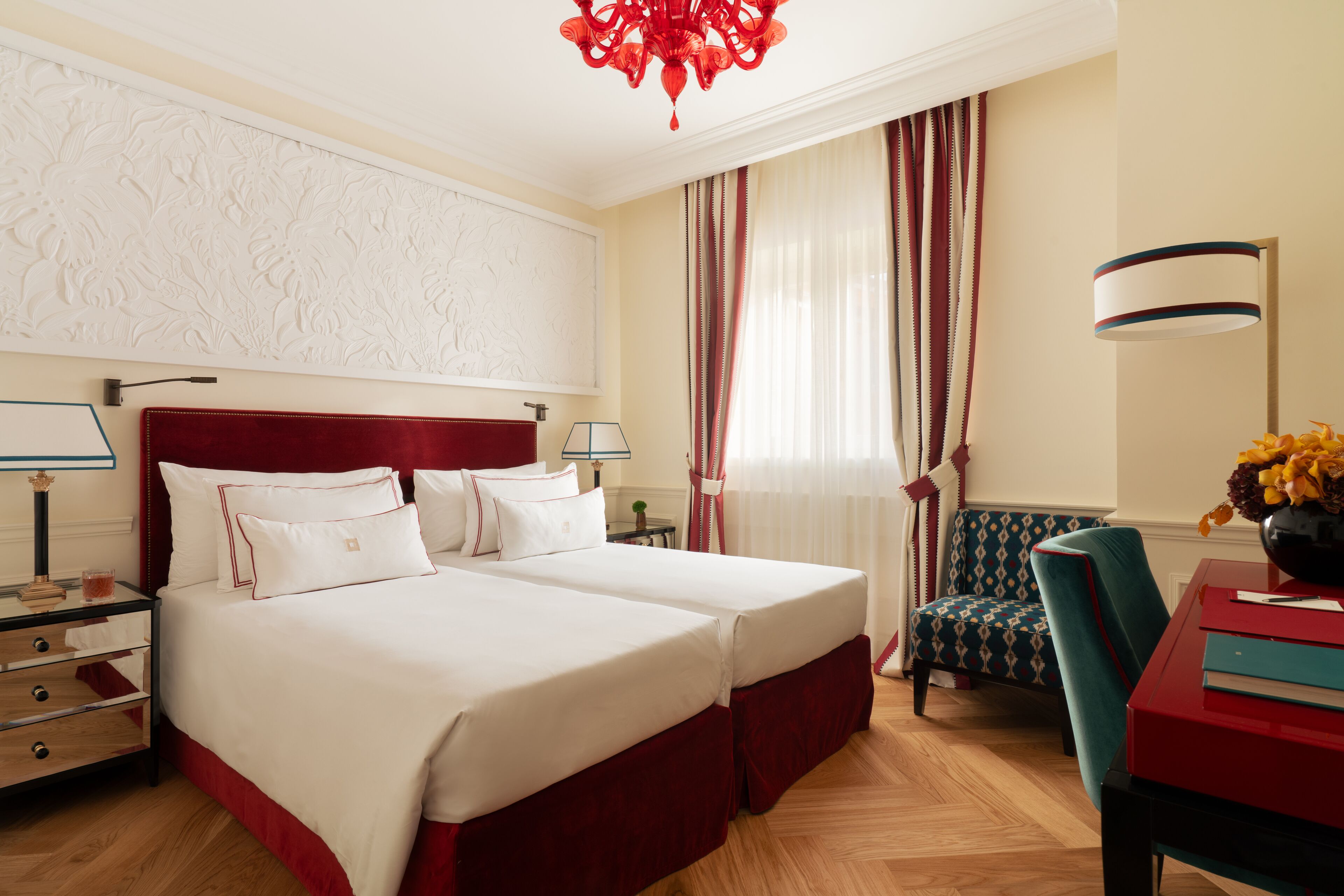 A hotel room with a large bed, a desk with a chair, a lamp, and a vase with flowers.