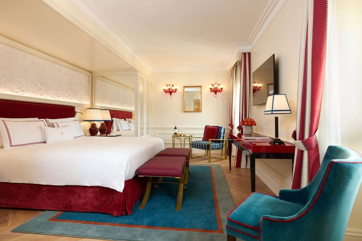 A hotel room with a large bed, a desk, a chair, a TV, and a red curtain.