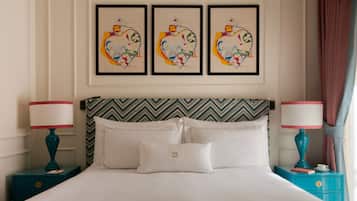 Habitación de hotel con cama, dos mesitas de noche, cabecera con estampado en zigzag, tres obras de arte enmarcadas en la pared y ventana con cortinas.