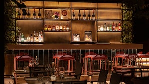 A dimly lit bar area with shelves of bottles and glasses, red chairs, and tables set for dining. - Palazzo Ripetta (Rome)