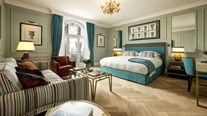 A well-appointed hotel room with a large bed, a sitting area with a sofa and armchair, a desk with a chair, and a chandelier. - Palazzo Ripetta (Rome)