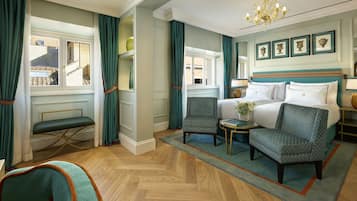 A hotel room with a large bed, two armchairs, a small table, and a view of the outside.