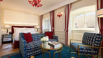 Habitación de hotel con cama, sofá, sillón, una mesita con un jarrón de flores y una araña.