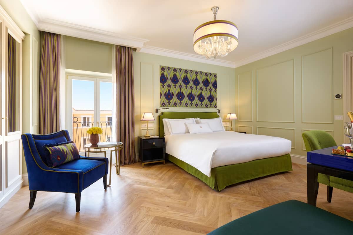 A hotel room with a large bed, a chair, a table, and a chandelier.