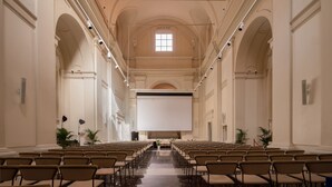 A large hall with rows of chairs, a projector screen, and a high ceiling with decorative moldings. - Palazzo Ripetta (Rome)