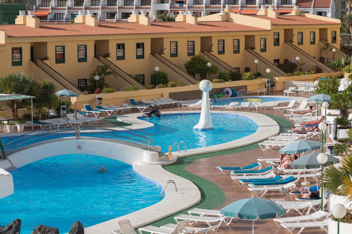 Un resort con varias piscinas, tumbonas y vistas de edificios hoteleros al fondo.