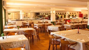 A restaurant with multiple tables and chairs, a kitchen in the background, and a wine rack.
