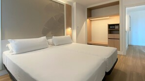 A modern hotel room with a large bed, built-in wardrobe, and a small kitchenette.