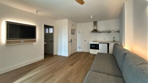 A modern living room with a large flat-screen TV mounted on the wall, a grey sofa, and a wooden ceiling fan.