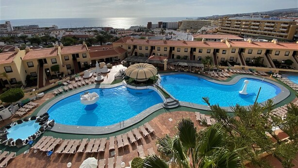 A resort with a large central pool, multiple smaller pools, and a view of the sea.