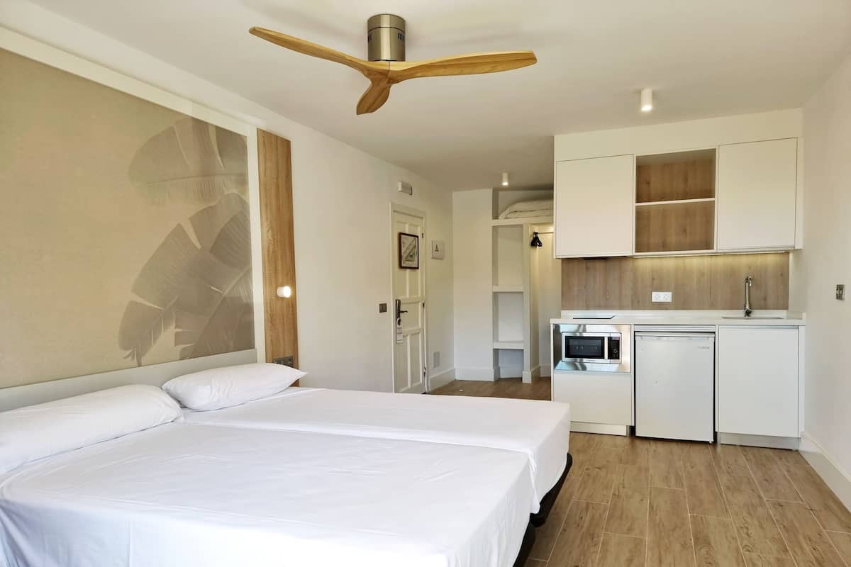 Habitación de hotel con una cama grande, ventilador de techo, kitchenette con microondas y lavavajillas, y piso de madera.