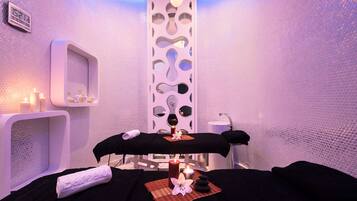 Een spa-ruimte met twee massagetafels, kaarsen, een spiegel en een wand met een structuur.