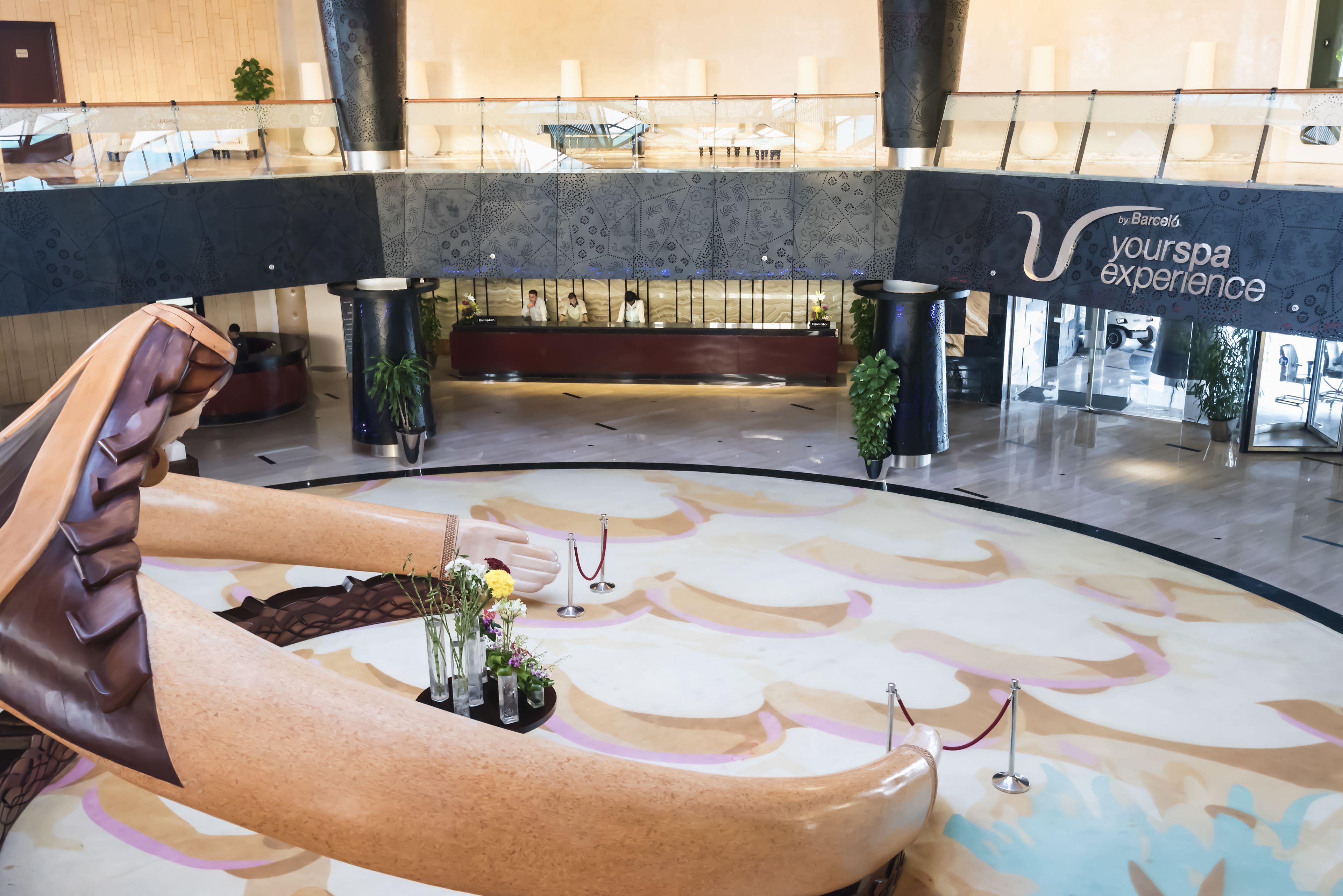 Un vaste atrium doté d’un espace de détente central, d’un comptoir d’accueil et d’une enseigne indiquant « Votre expérience spa ».