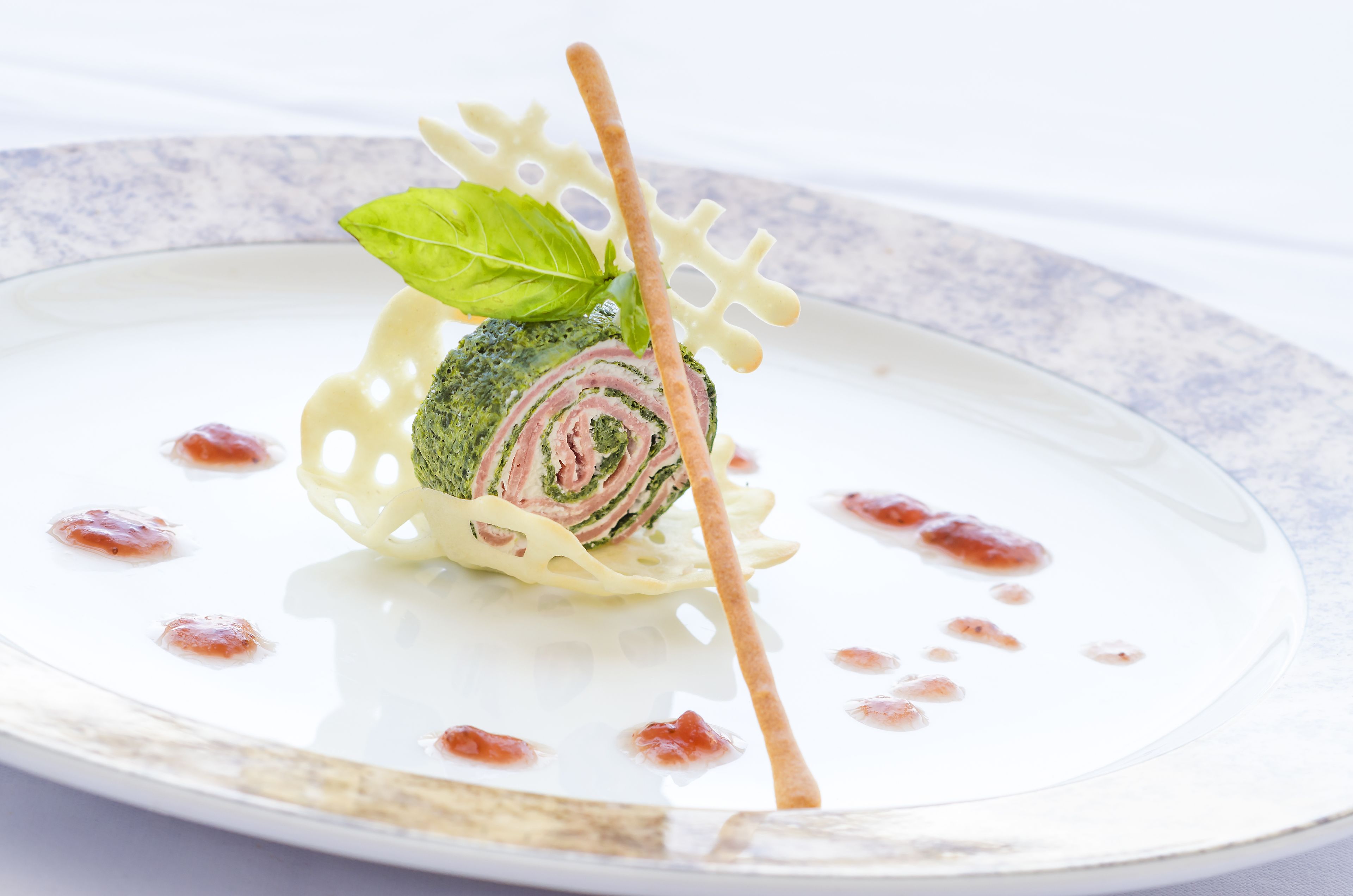 A rolled appetizer with a basil leaf garnish on a white plate with a blue rim.
