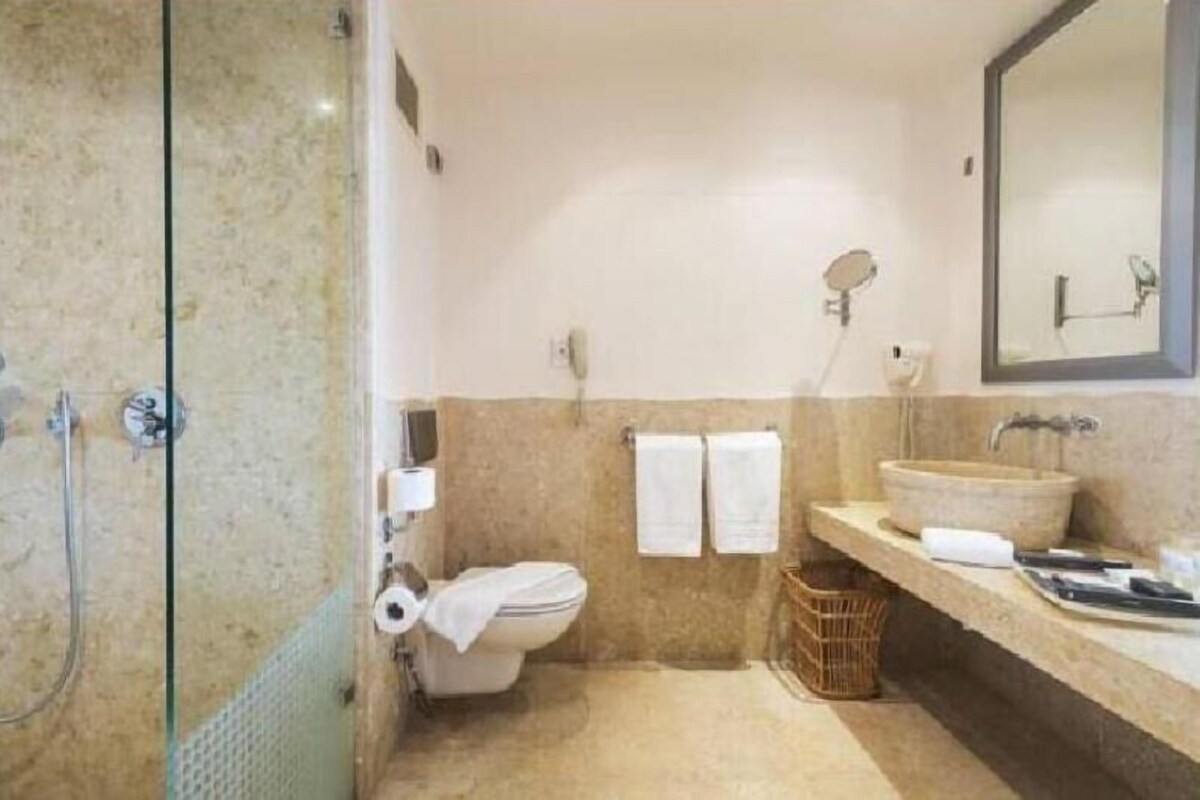 A bathroom with a glass shower enclosure, a toilet, a sink, and a mirror.