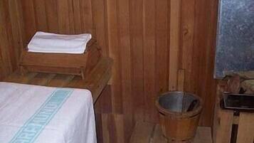 Una habitación de madera con una cama, una mesita de madera y un balde.