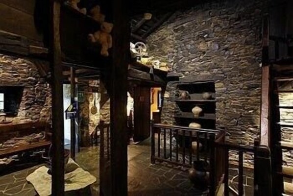 A rustic stone-walled room with a wooden staircase, a small window, and shelves with decorative items.