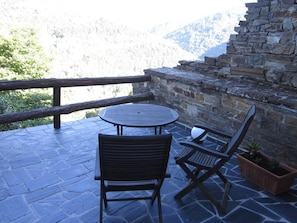 A stone patio with a round table and two chairs, overlooking a mountainous landscape. - Hotel La Rectoral (Taramundi)