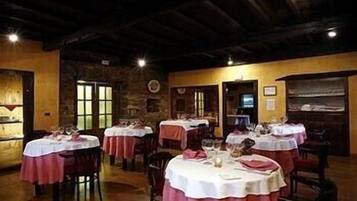 Un restaurante con mesas redondas cubiertas con manteles blancos y servilletas rojas, sillas de madera y una pared de piedra al fondo.