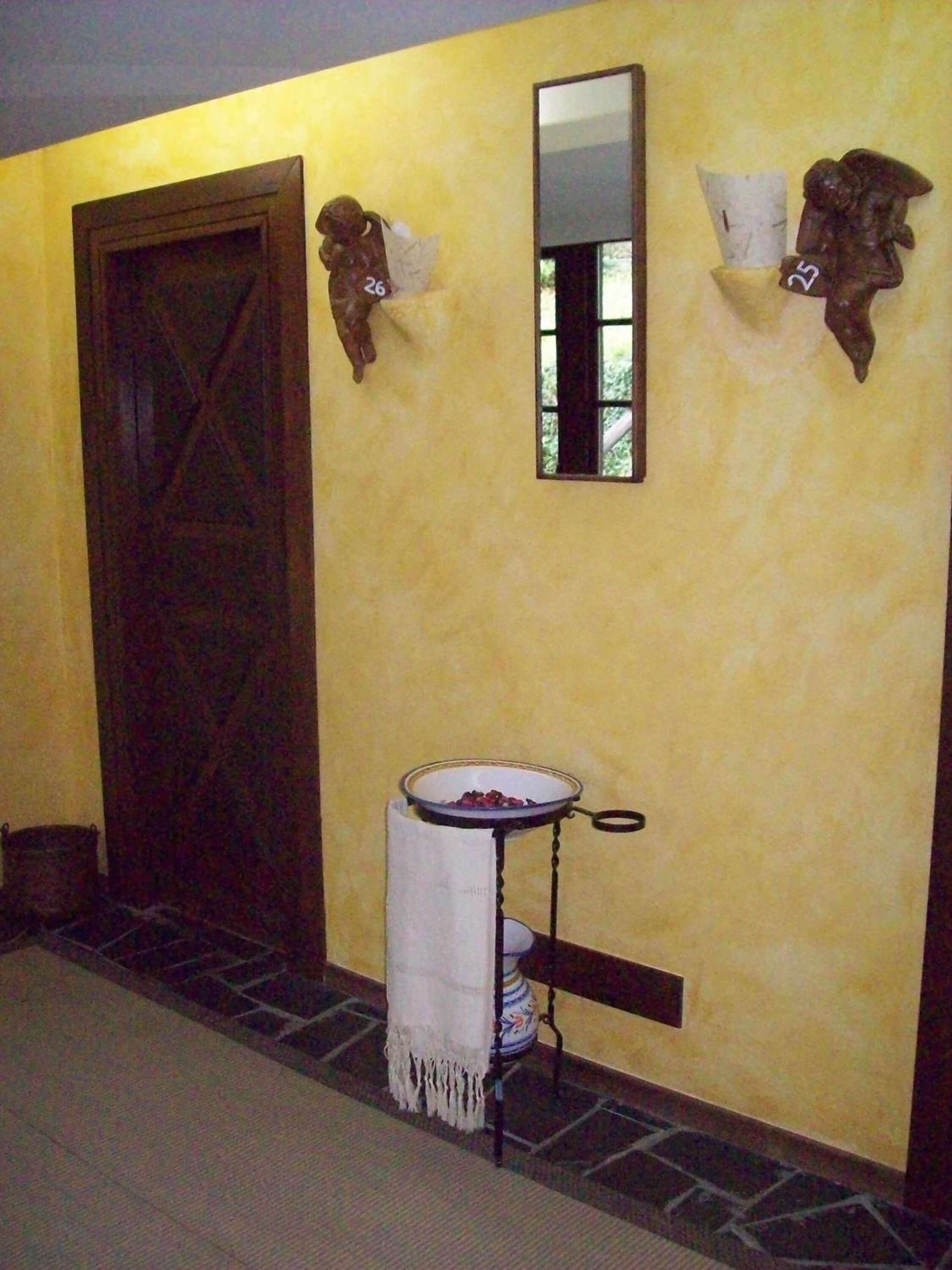 Una habitación con puerta de madera, una ventana pequeña, un espejo fijado a la pared y una repisa metálica con un cuenco.