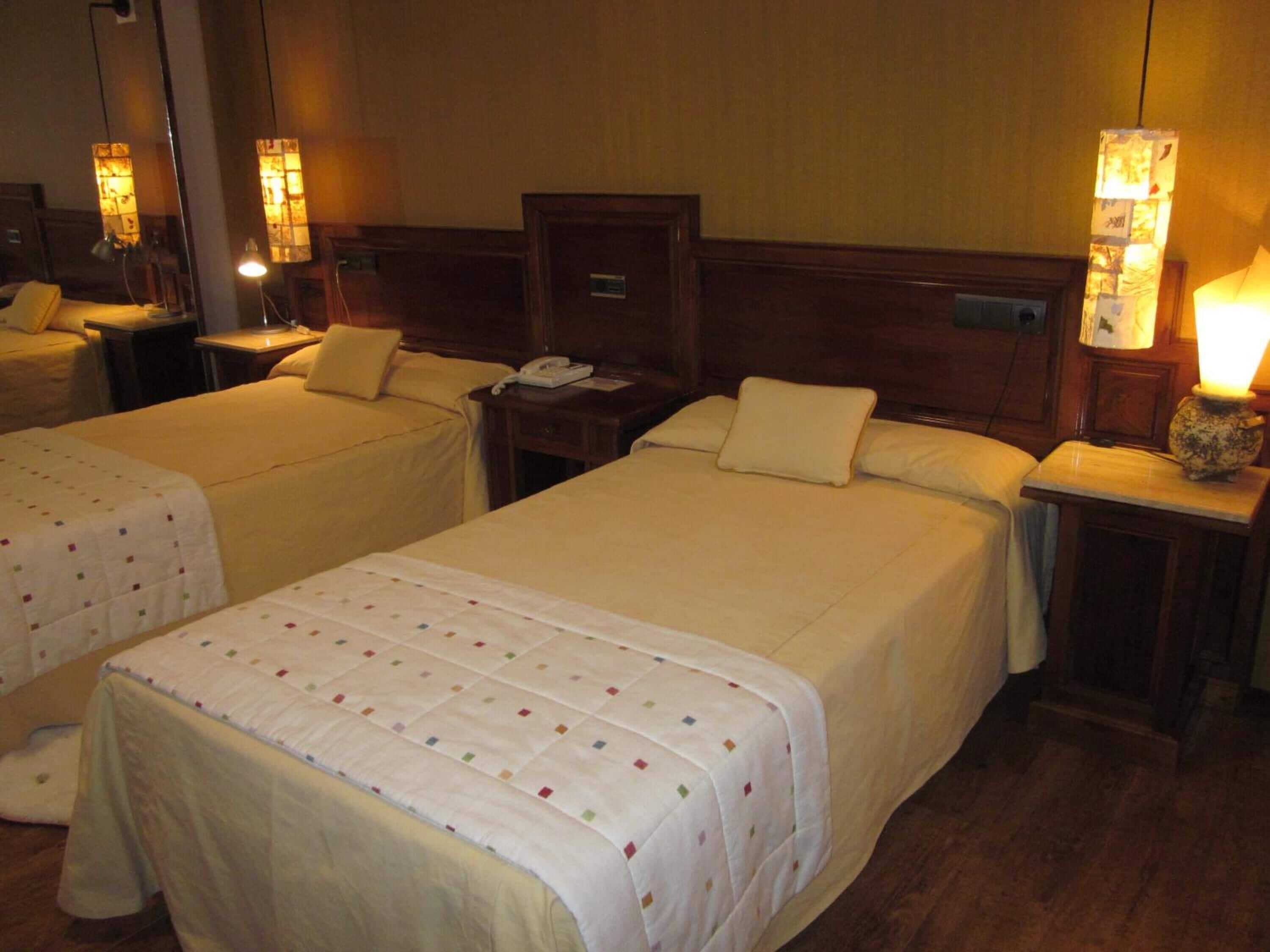 Habitación de hotel con dos camas, cada una con cabecero de madera, mesitas de noche con lámparas y un mesillero con teléfono.