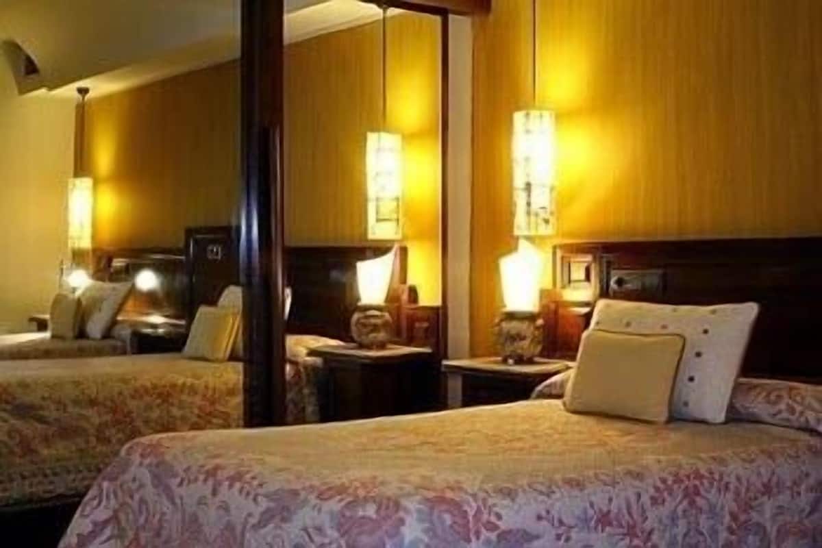 A hotel room with two beds, wooden headboards, and bedside lamps.