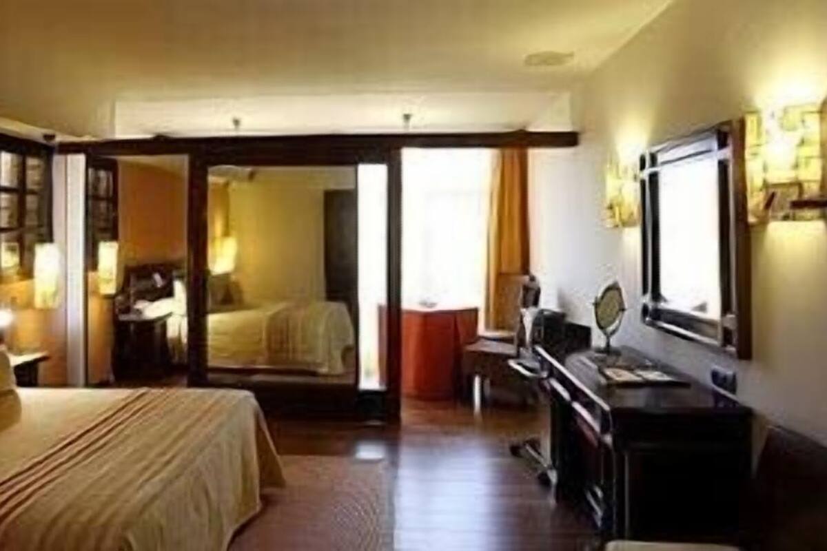 A hotel room with a bed, a desk, a chair, a TV, and a mirror.