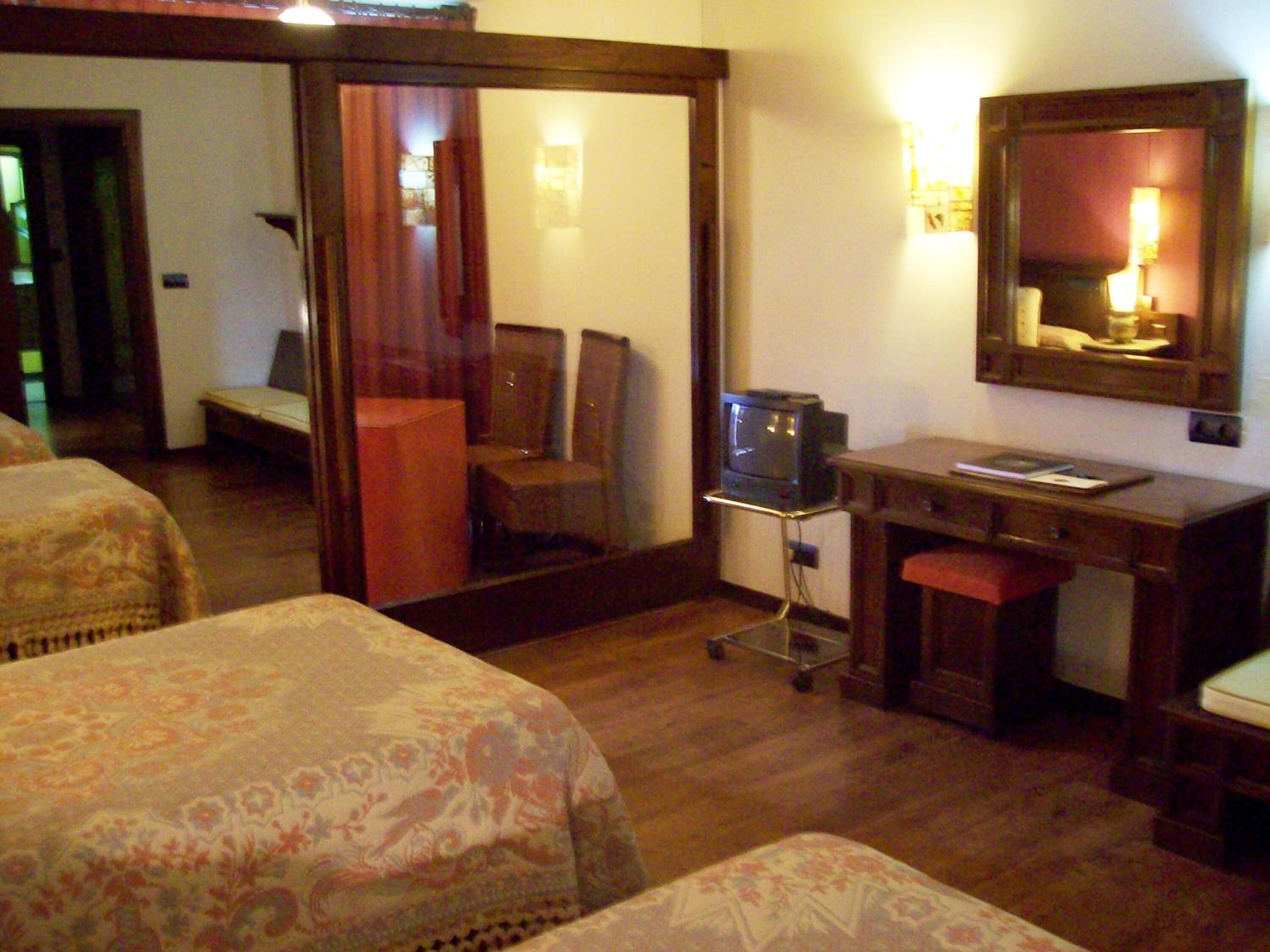 Een hotelkamer met twee bedden, een bureau, een stoel, een televisie en een spiegel.