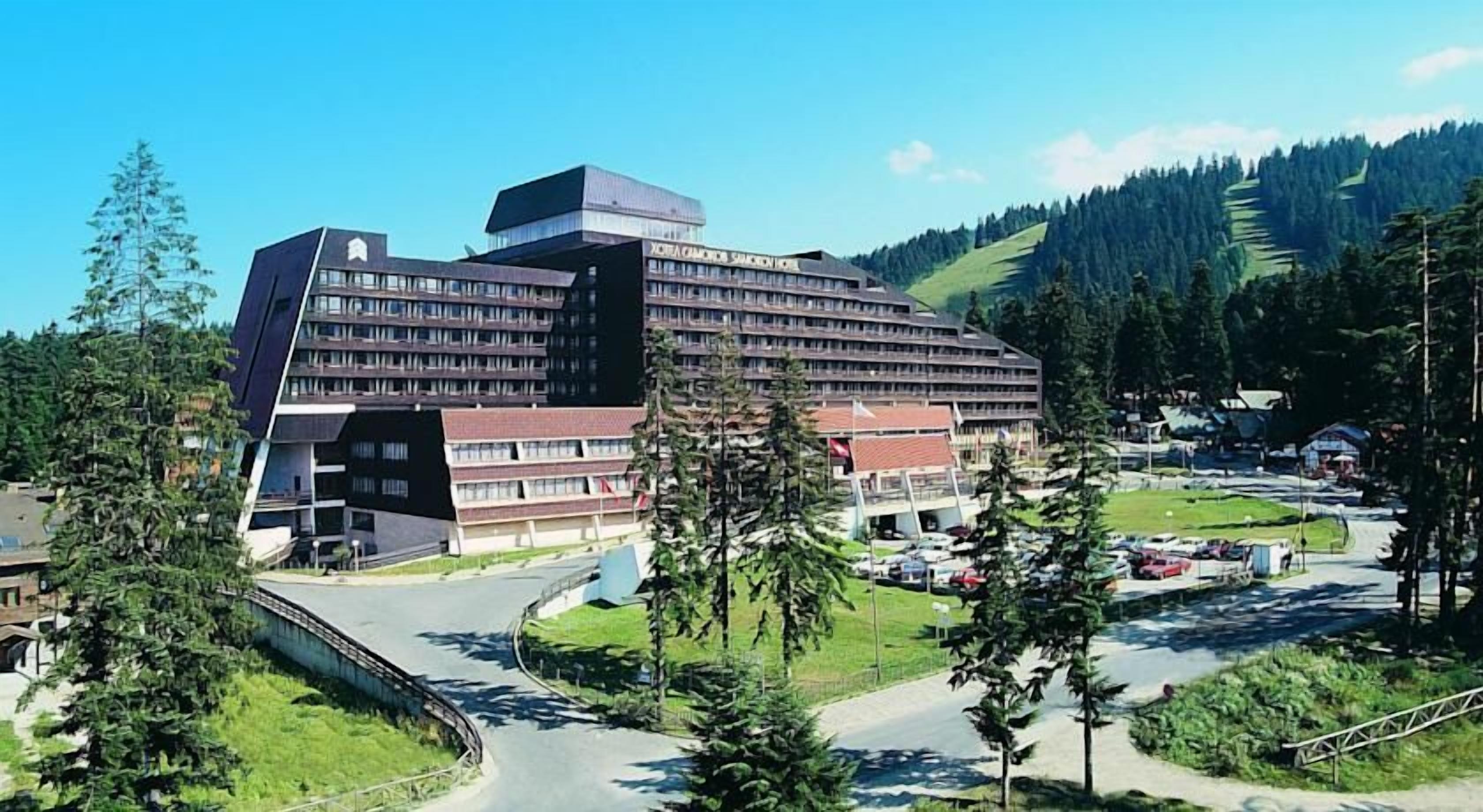 A modern hotel with a unique angular design, surrounded by a lush green landscape and a clear sky.