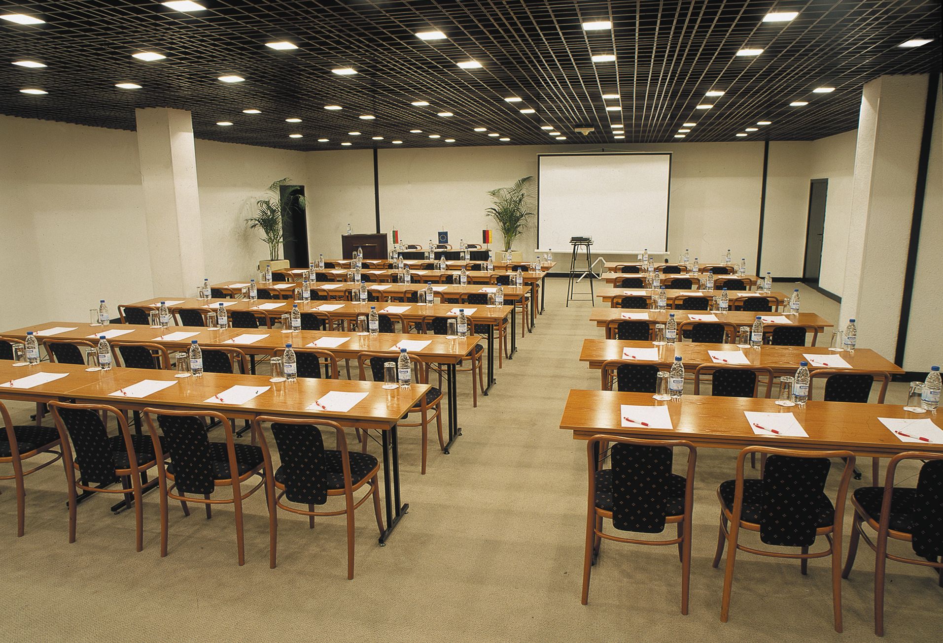 Una sala de conferencias con varias mesas y sillas, equipada con botellas de agua y documentos.