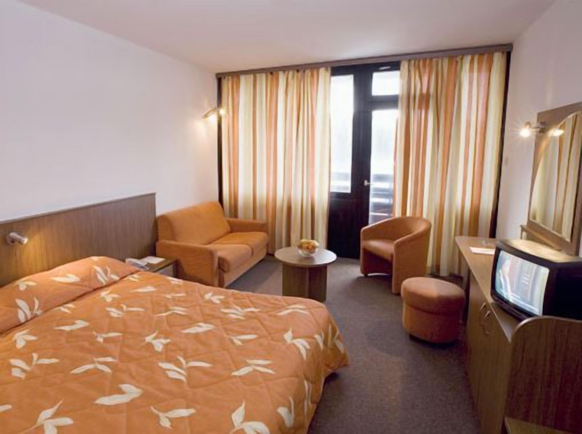 Una habitación de hotel con cama, dos sillones, una mesita, televisión y ventana con cortinas.