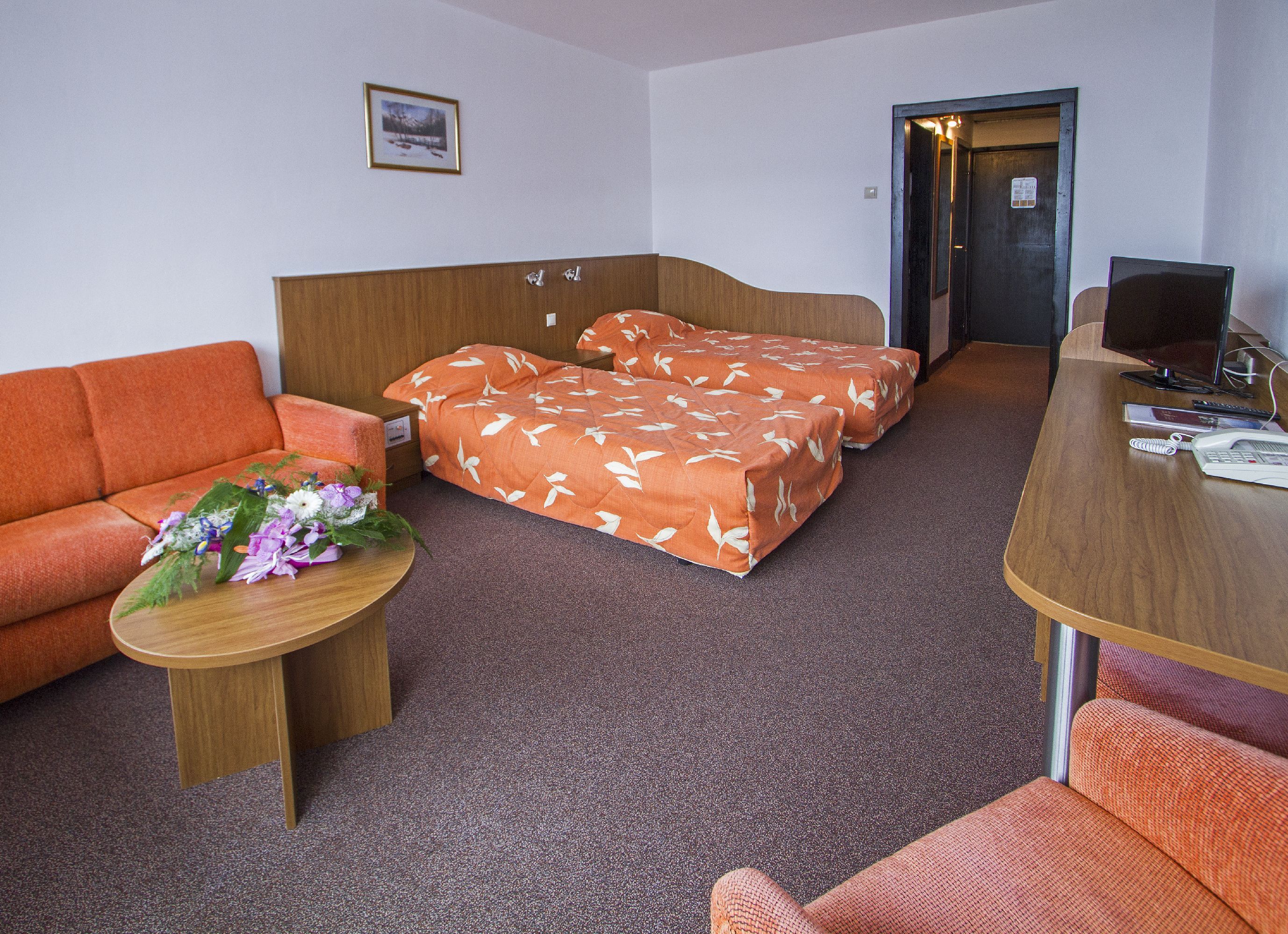 Une chambre d’hôtel avec un canapé, deux lits avec des couvre-lits assortis, un bureau avec un ordinateur et un téléphone.