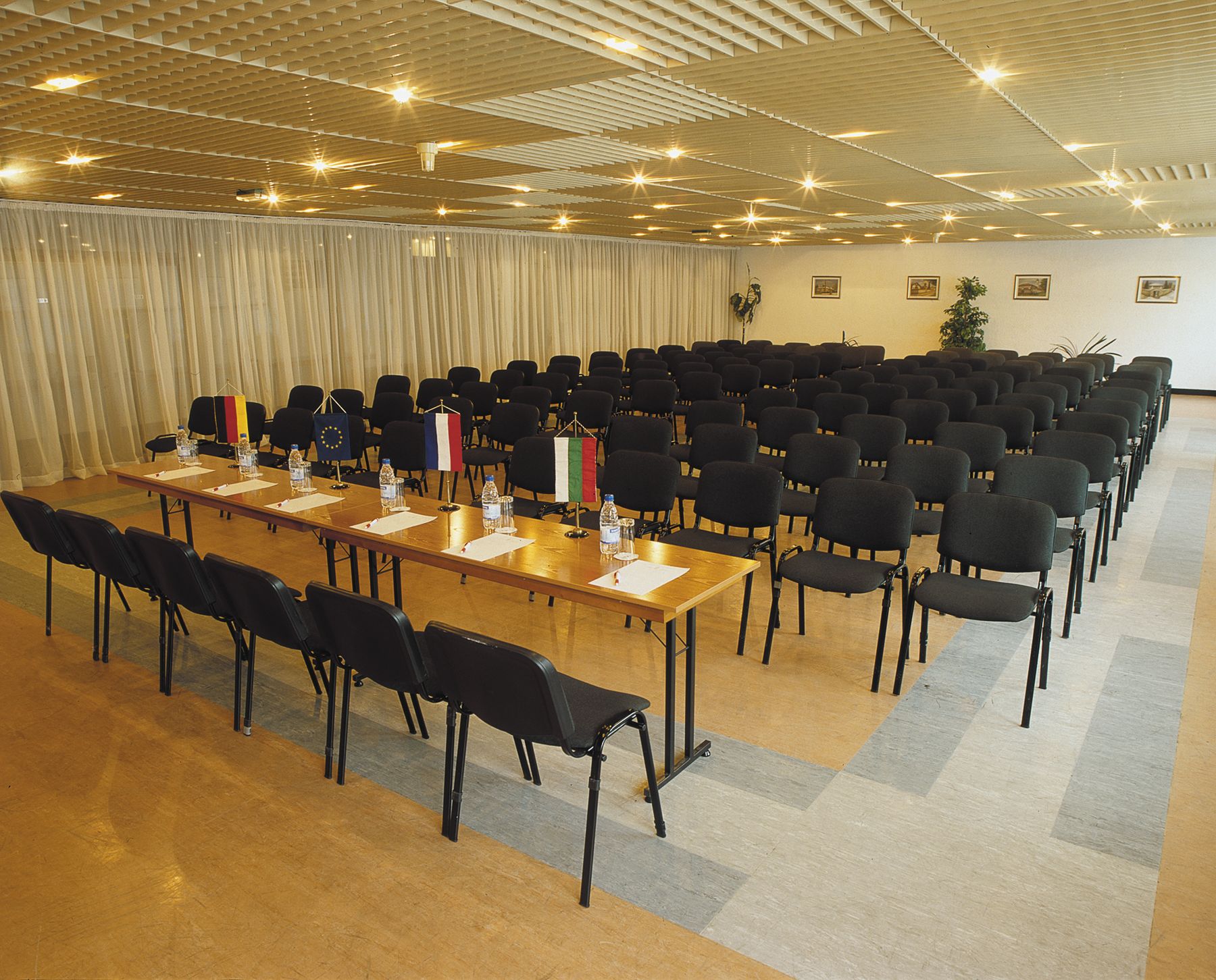 A conference room with a long table, rows of chairs, and flags.