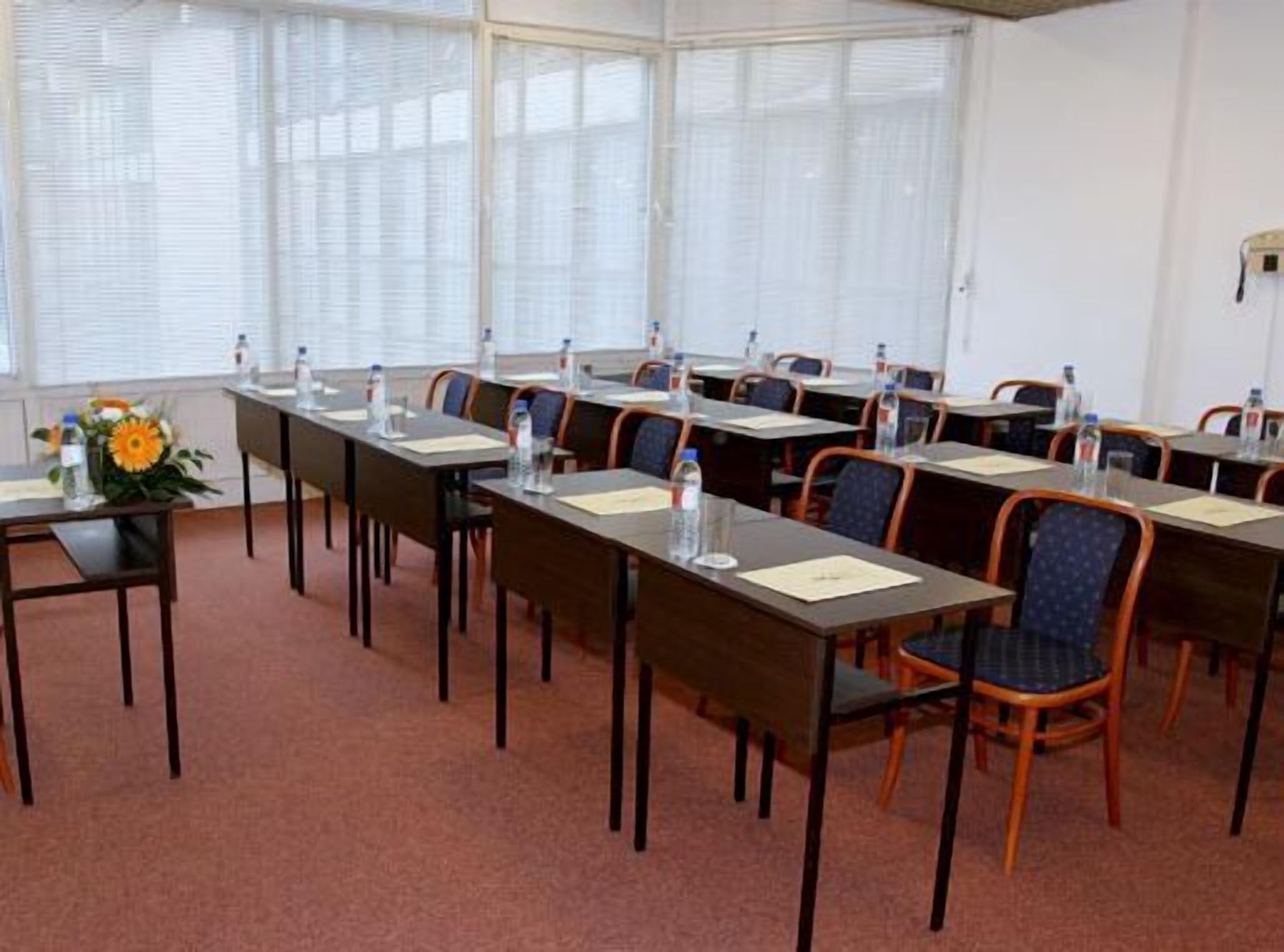 Een vergaderzaal met lange tafels, stoelen en waterflessen.