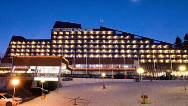 A multi-story hotel with numerous illuminated windows, a ski lift in the foreground, and a snow-covered ground. - Hotel Samokov (Samokov)