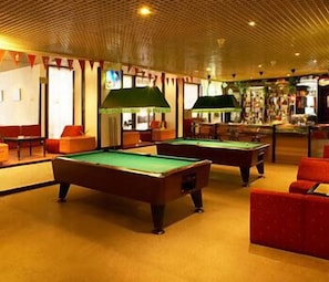 A pool table with a green felt surface, surrounded by red chairs, in a room with a patterned ceiling and warm lighting. - Hotel Samokov (Samokov)