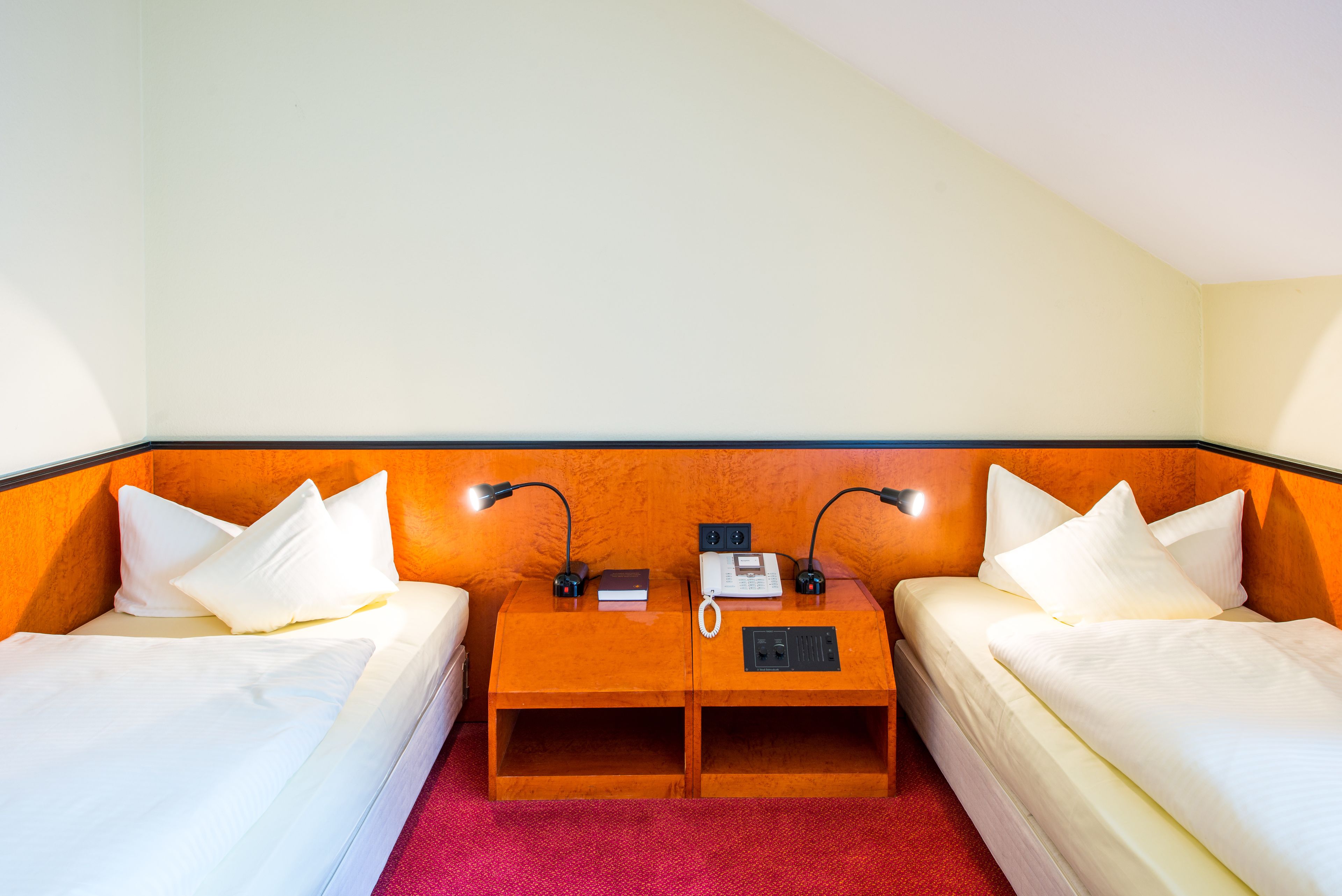 A hotel room with two single beds, a wooden nightstand, a telephone, and two lamps.