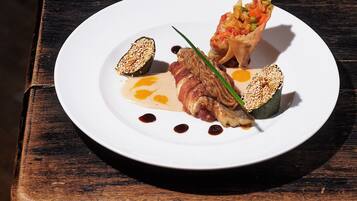 Un plato blanco con diversos alimentos, incluyendo un trozo de carne, verdura y un recipiente pequeño con salsa.