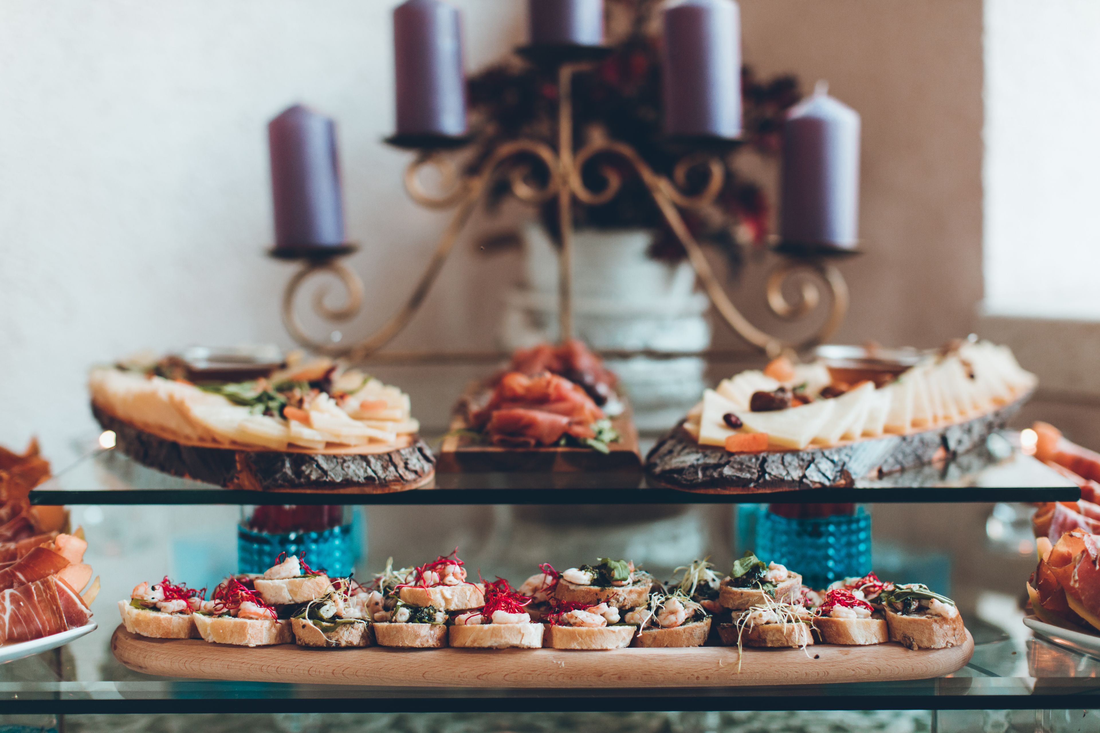 A buffet with various food items on glass and wooden serving boards, a decorative candle holder, and a blue glass candle.