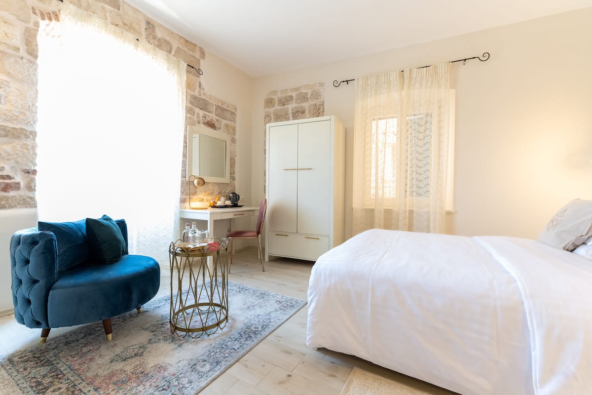 A bedroom with a bed, a desk with a chair, a blue armchair, and a wardrobe.