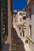 Una estrecha calle de piedra con un cartel de hotel, edificios de piedra y un cielo azul despejado.