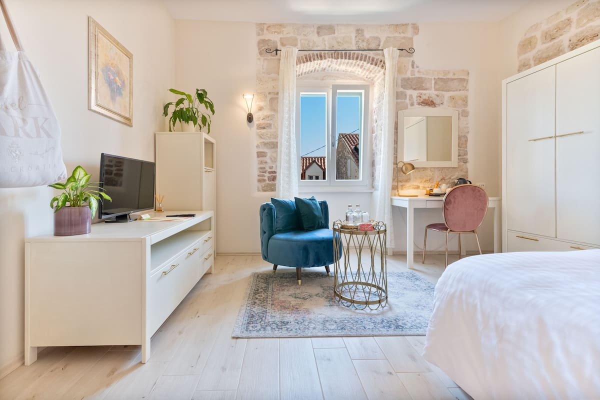 A bedroom with a bed, a desk with a computer, a chair, a small table, and a wardrobe.