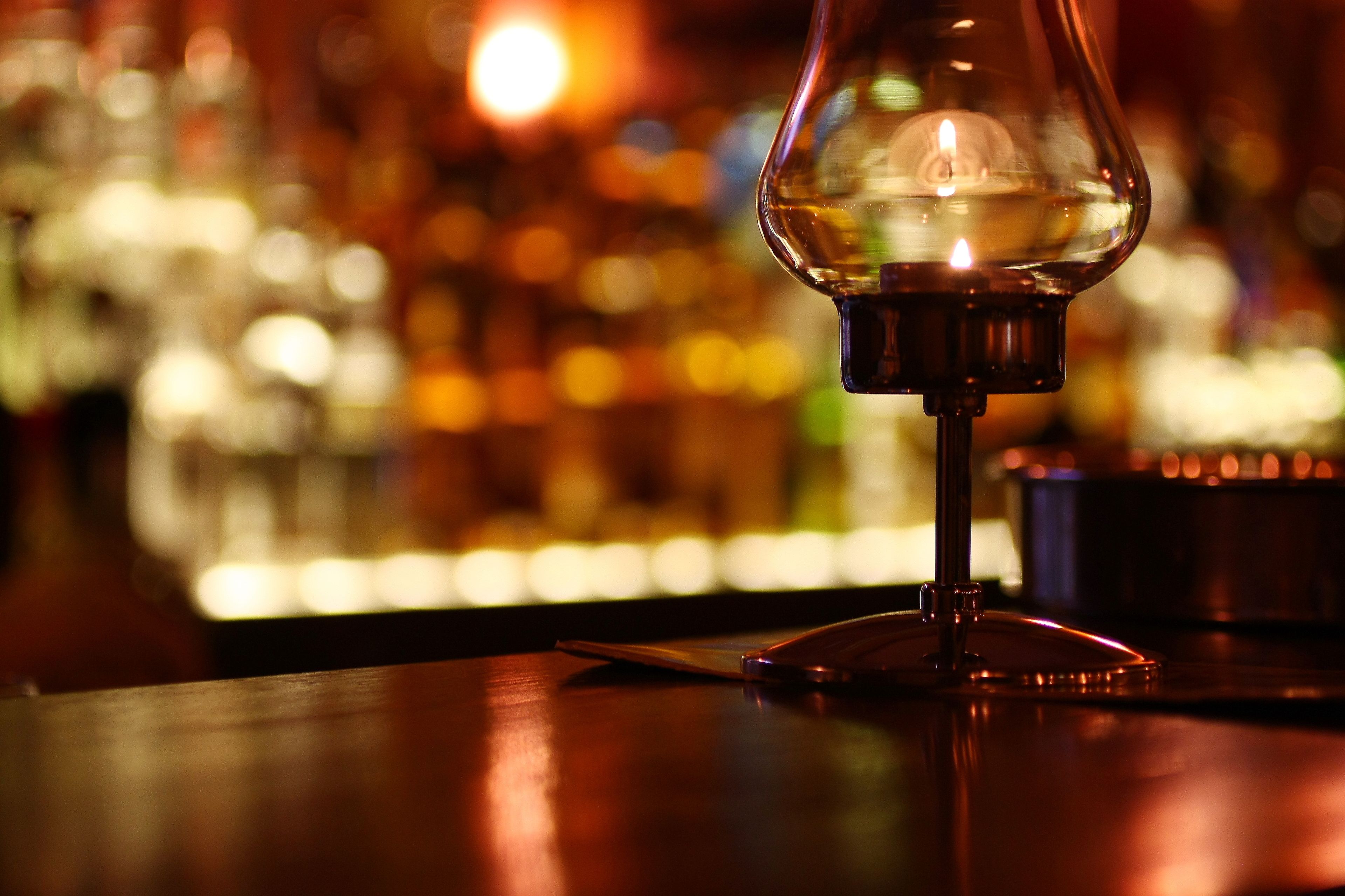 En närbild på ett glas med en vätska, troligen en drink, på en bardisk med en suddig bakgrund av ljus.