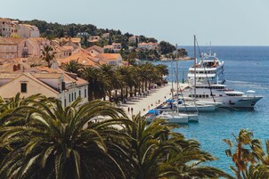 Un pueblo costero con un puerto deportivo, barcos y una hilera de edificios con tejados rojos.
