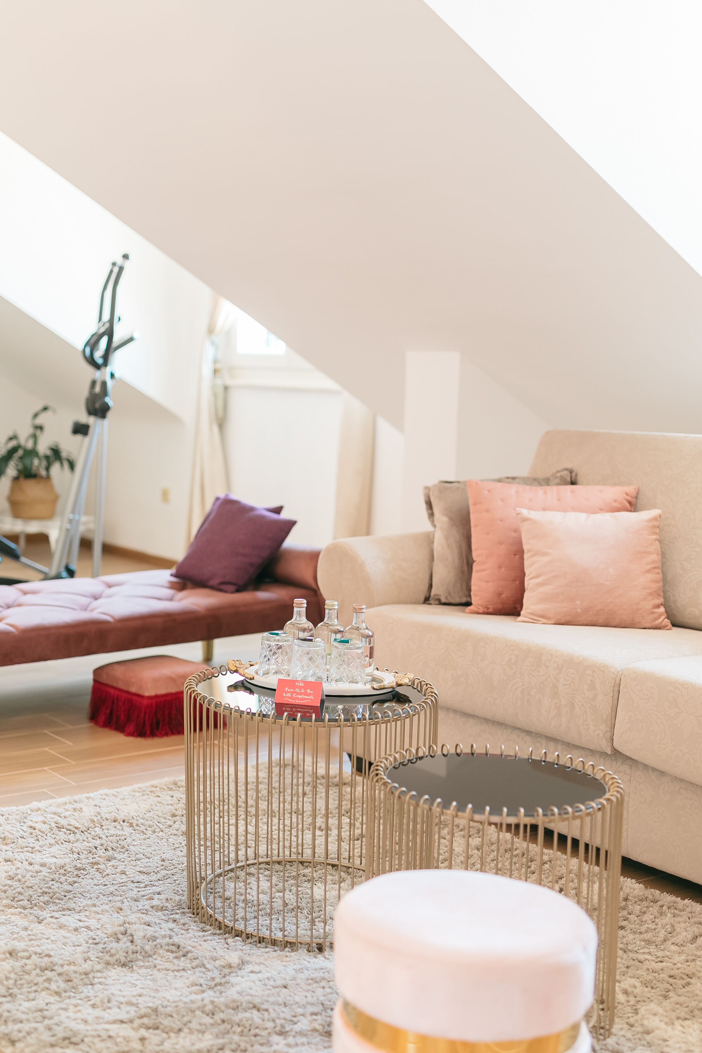 Una sala de estar acogedora con sofá, reposapiés y mesa de centro, con una planta y una escalera al fondo.