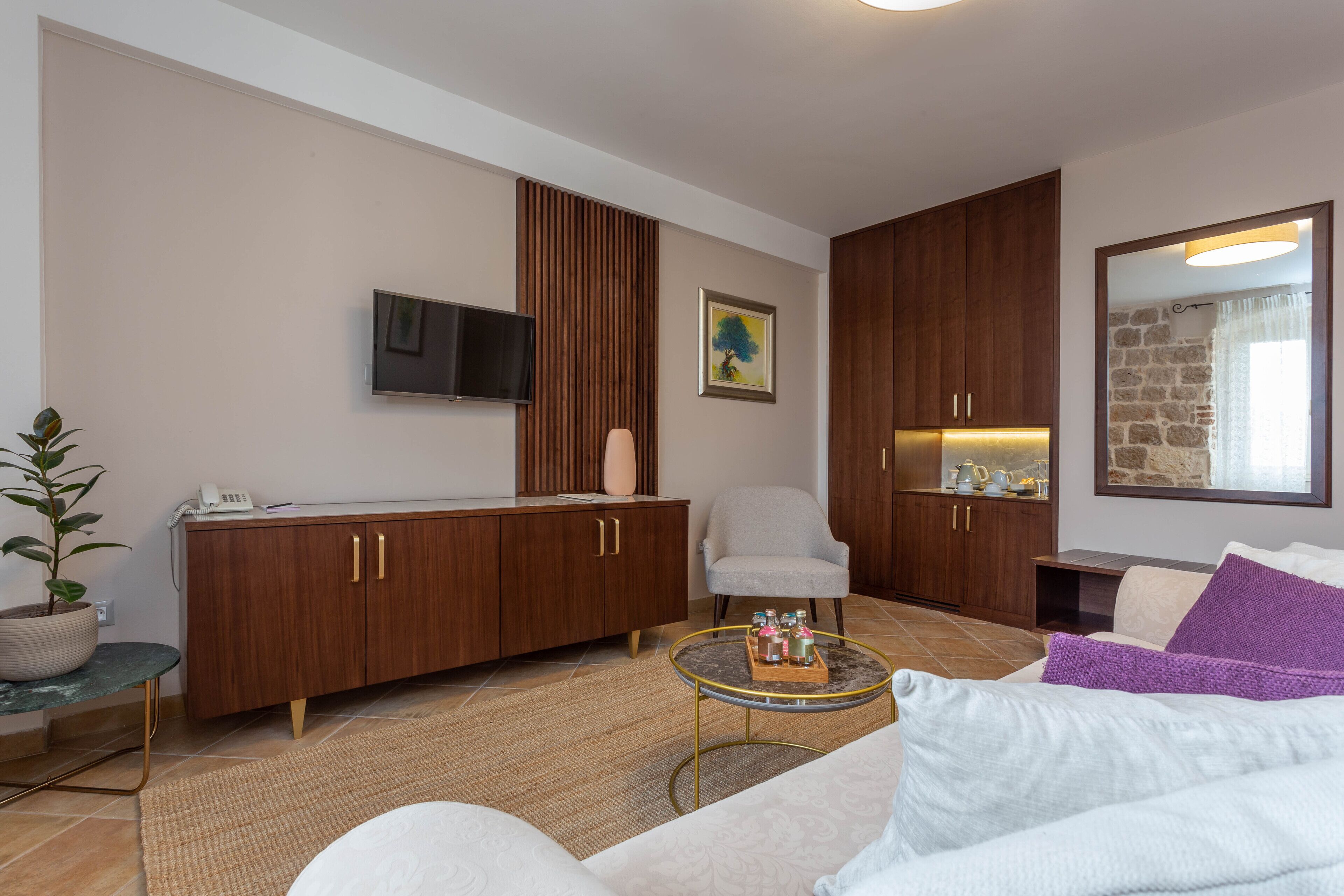 A modern living room with a sofa, armchair, wooden cabinet, TV, and a potted plant.
