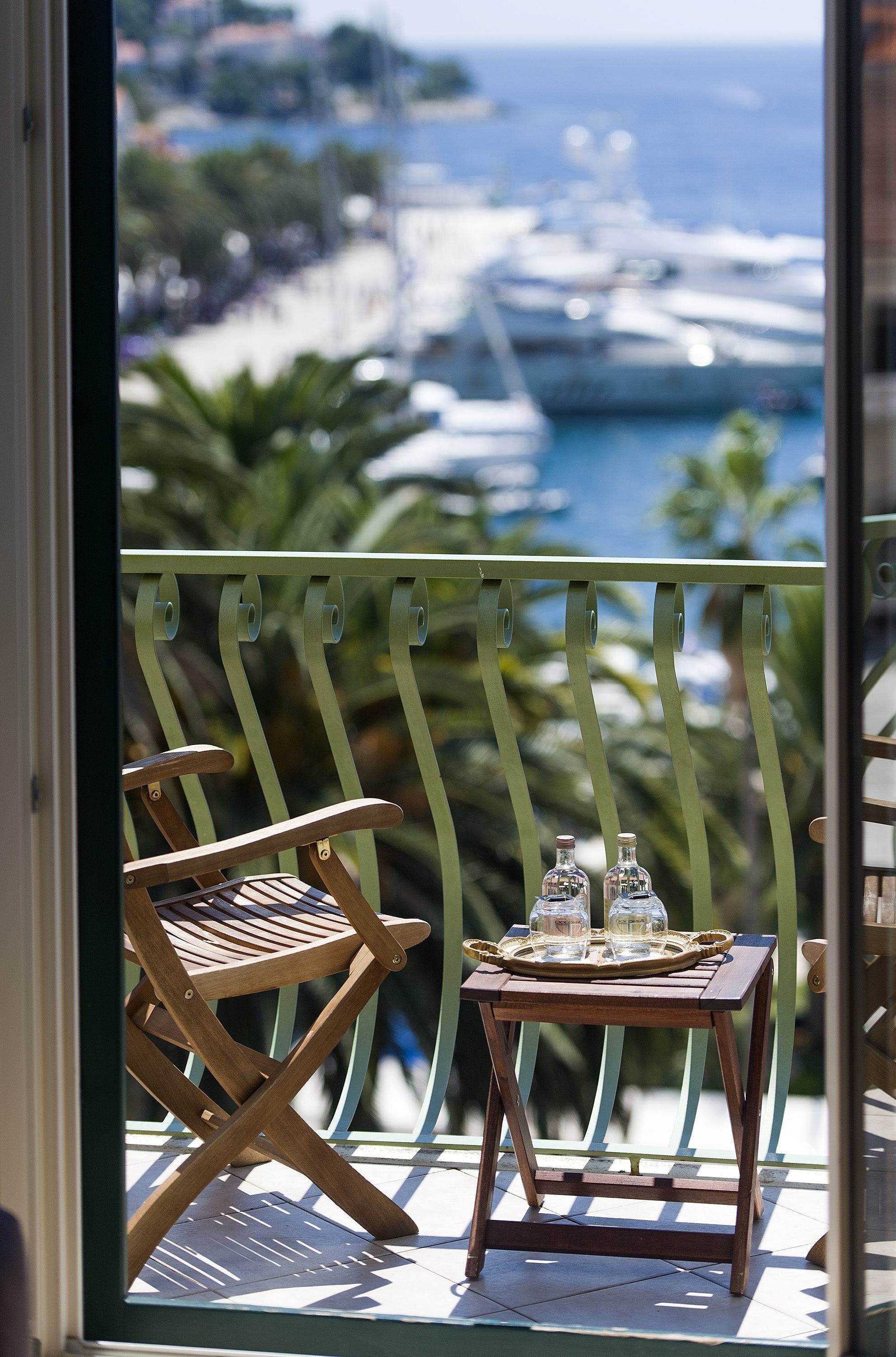 A balcony with a wooden chair and a small table with two bottles and glasses.